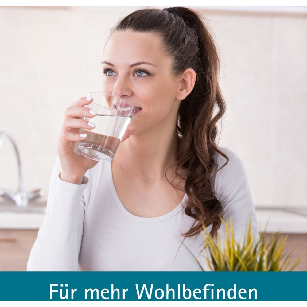 Frau trinkt Wasser aus Glas. Text: Für mehr Wohlbefinden. Hintergrund: Küche mit Pflanze.