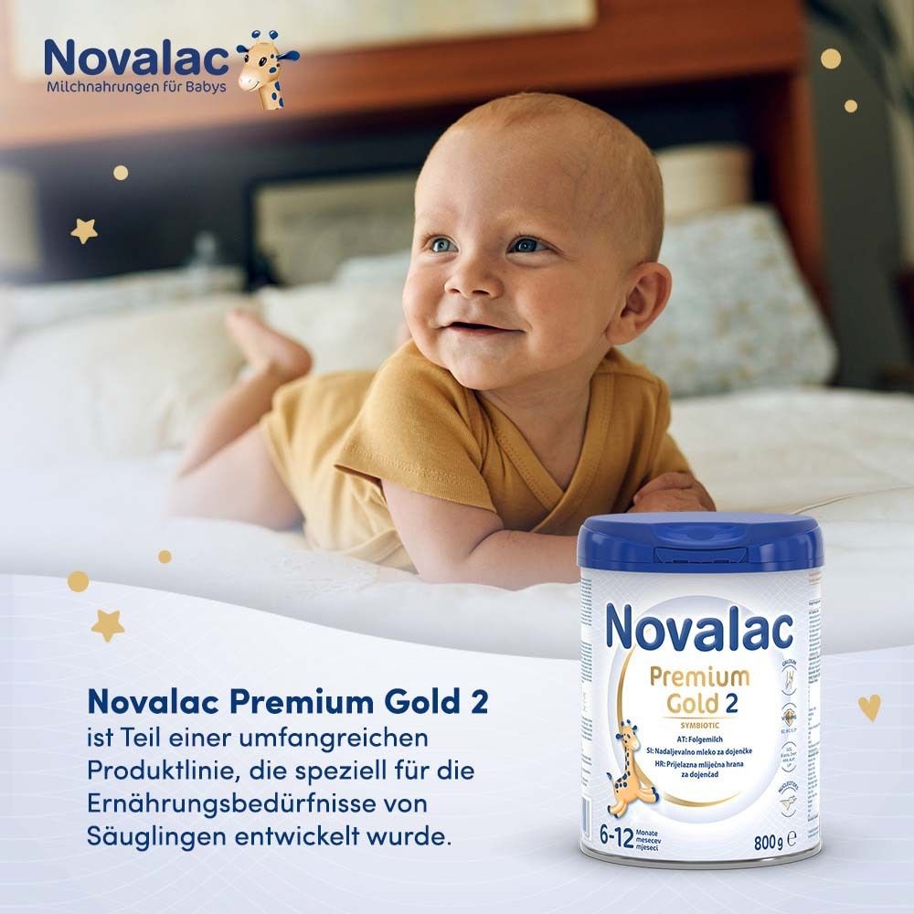 Baby liegt auf dem Bett neben einer Dose Novalac Premium Gold 2. Dose mit blauem Deckel und weißem Etikett.