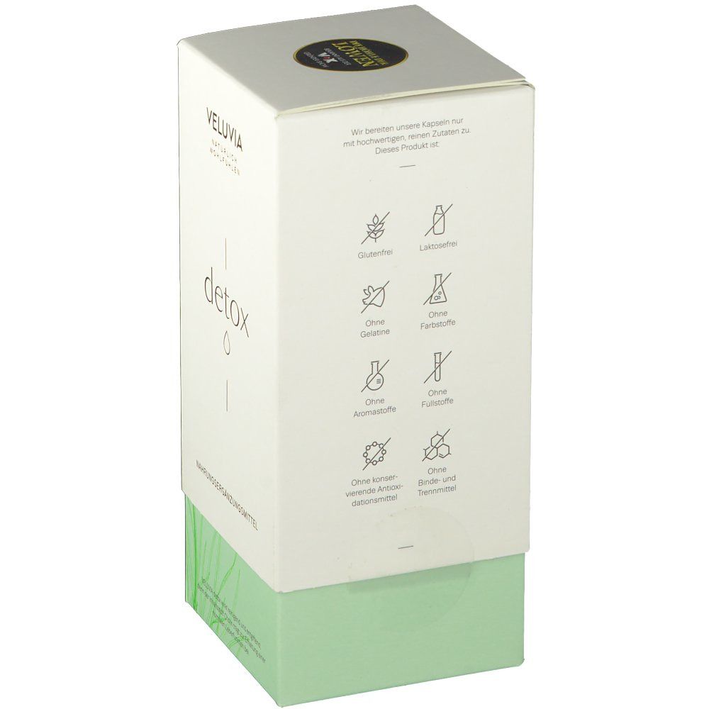 Weiße Produktverpackung mit grüner Basis. Aufschrift VELUVIA Detox. Symbole für 'ohne' Inhaltsstoffe. Oben ein goldfarbenes Logo.