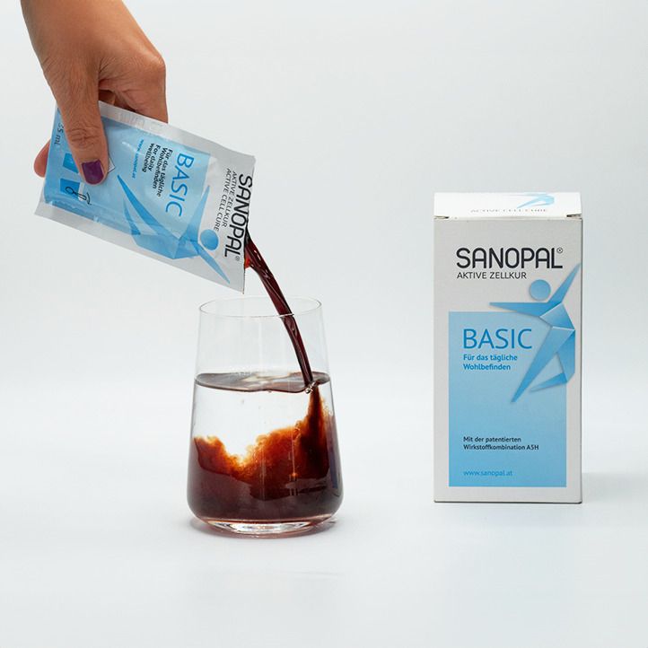 Hand gießt Flüssigkeit aus einem Beutel in ein Glas. Auf dem Beutel steht SANOPAL BASIC. Daneben steht die Produktverpackung.