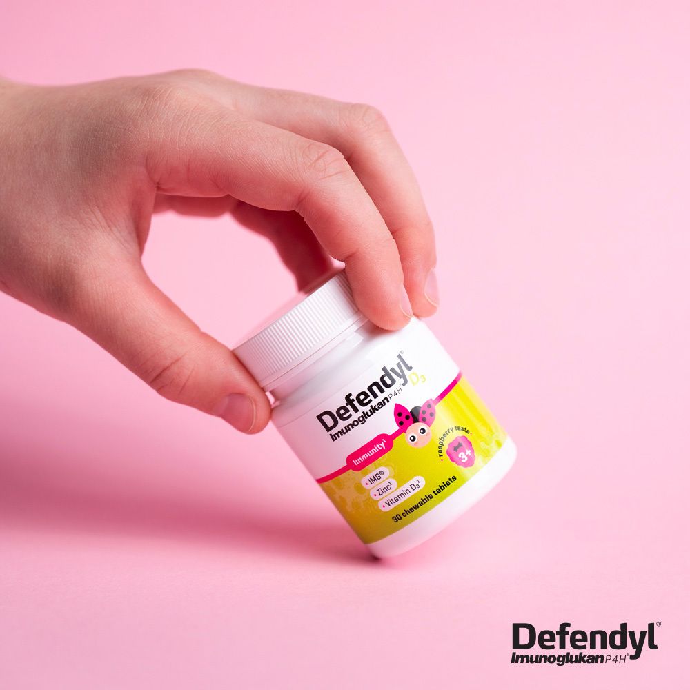 Hand hält Flasche Defendyl-Imunoglukan P4H D₃. Rosa Hintergrund. Flasche mit Tabletten.
