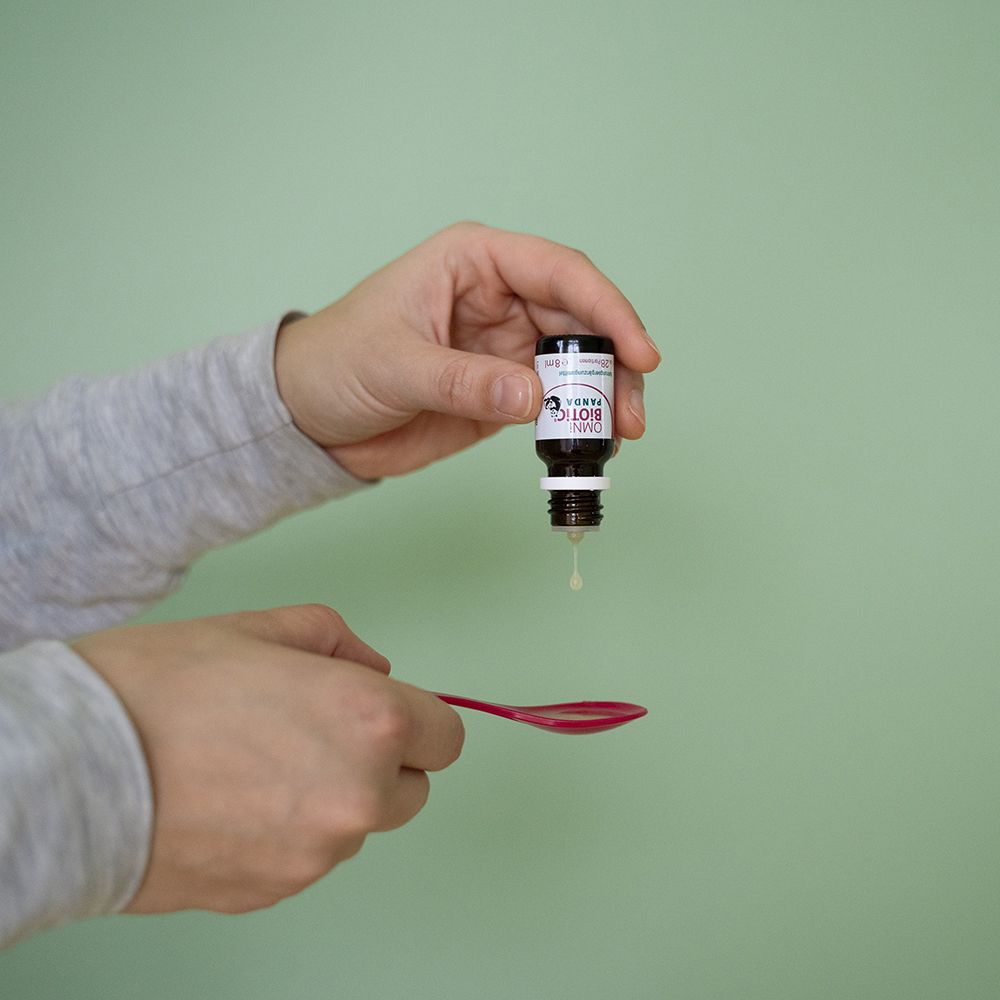 Eine Hand tropft OMNi-BiOTiC® PANDA aus einer kleinen Flasche auf einen roten Löffel.