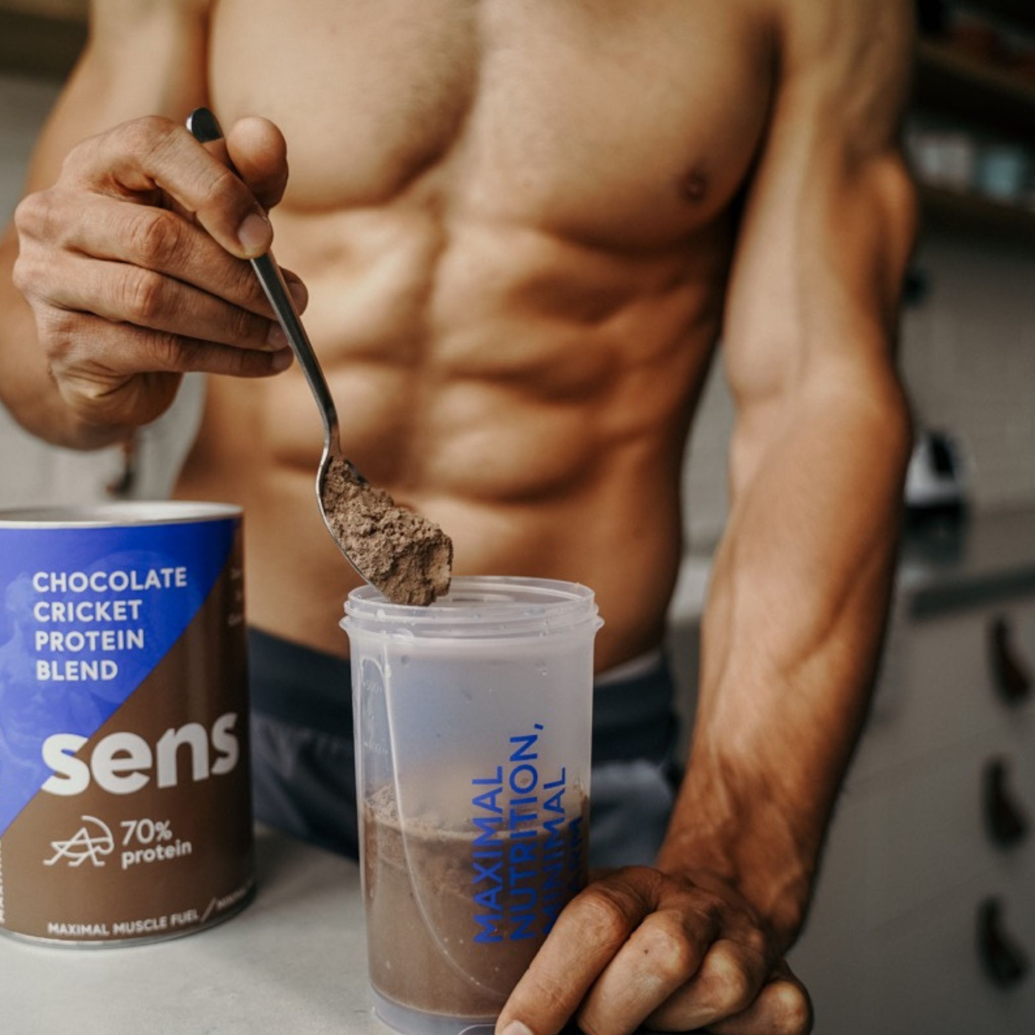 Person hält Löffel mit Protein Shake über Becher. Dose Sens Protein Shake daneben. Aufschrift: Chocolate Cricket Protein Blend.