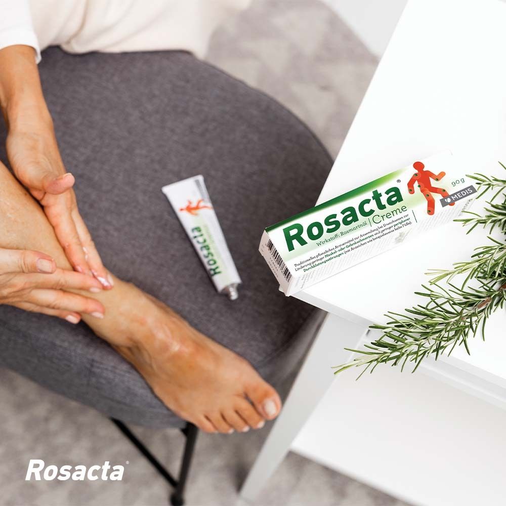 Person trägt Rosacta® Creme auf den Fuß auf. Tube und Verpackung liegen auf einem Tisch.