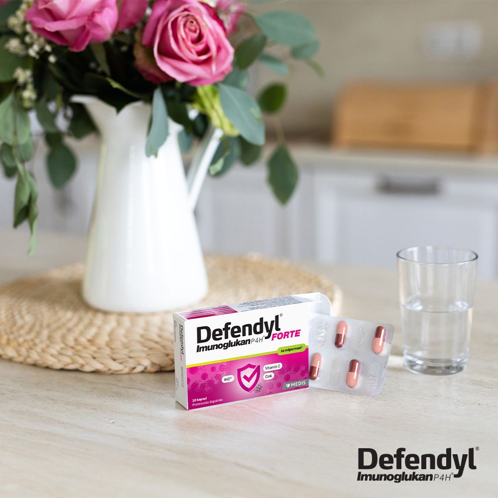 Defendyl-Imunoglukan P4H FORTE Packung und Blisterpackung auf einem Tisch. Blumen und Glas Wasser.