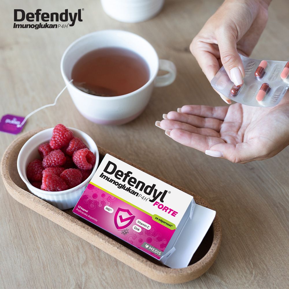 Hand nimmt Kapseln aus Blister. Defendyl-Imunoglukan P4H FORTE Packung, Himbeeren und Tee.
