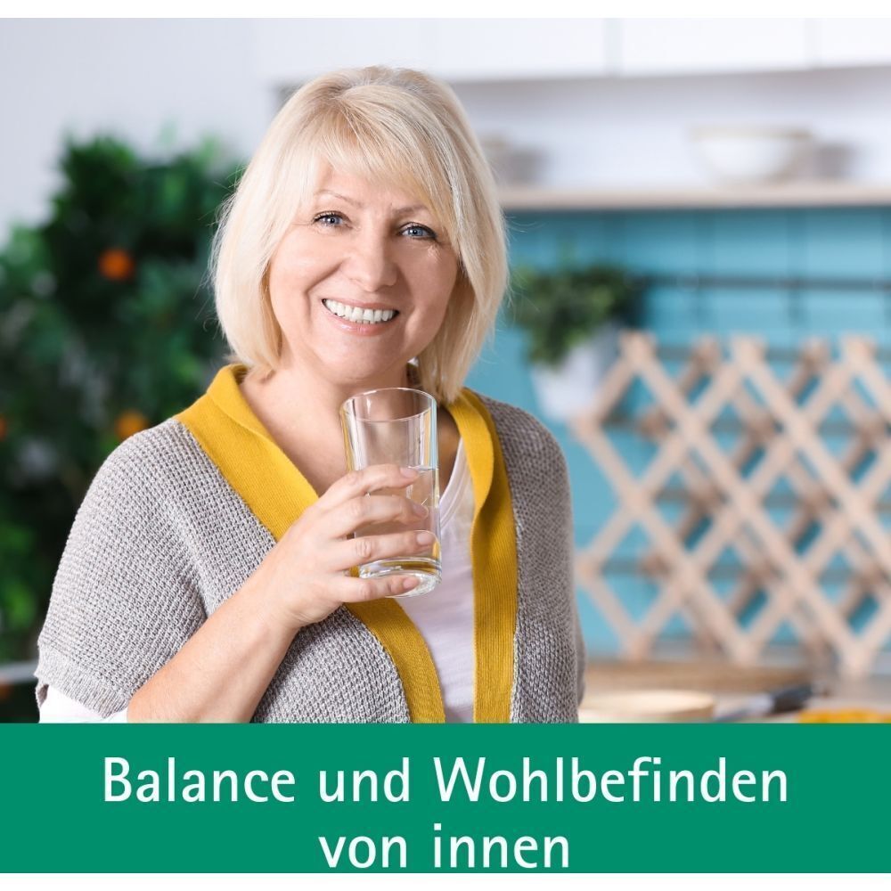 Lächelnde Frau mittleren Alters trinkt ein Glas Wasser, mit Text über Balance und Wohlbefinden.