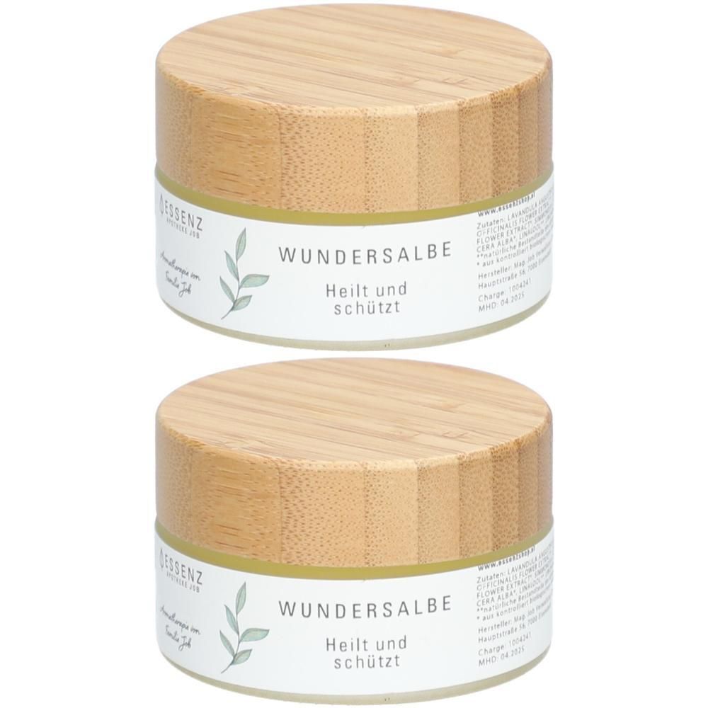 Zwei Gläser Wundersalbe mit Holzböden und Etiketten, die 'Heilt und schützt' angeben.