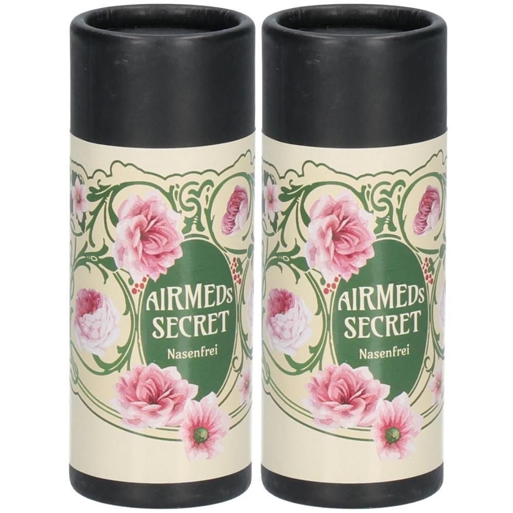 Zwei zylindrische Behälter mit schwarzem Deckel. Aufschrift: AIRMEDS SECRET Nasenfrei, umgeben von floralem Design mit rosa Blüten.