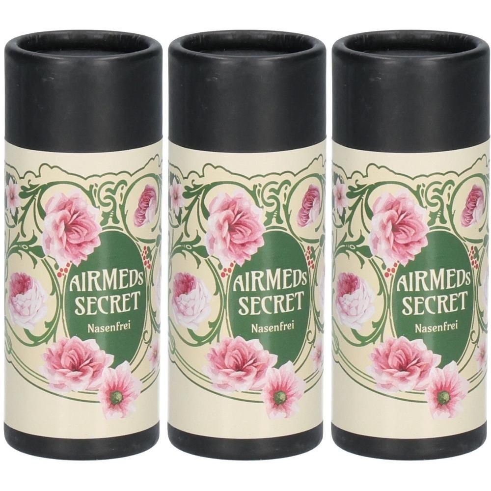 Drei zylindrische Behälter mit schwarzem Deckel. Aufschrift: AIRMEDS SECRET Nasenfrei. Floral-Design mit rosa Blüten.