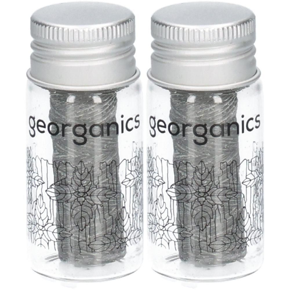 Zwei Glasbehälter mit Aktivkohle-Zahnseide und silbernen Schraubverschlüssen. Auf den Behältern ist das Logo 'georganics' und eine Blattzeichnung.