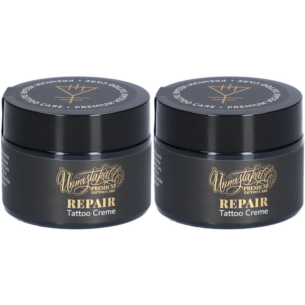 Zwei schwarze Tiegel mit goldfarbener Schrift. Aufschrift: Unmistakable, REPAIR Tattoo Creme. Deckel mit Logo und Schriftzug.