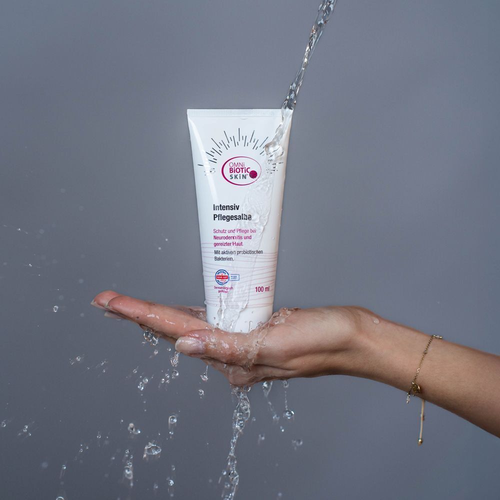 Weiße Tube OMNi-BiOTiC SKiN Intensiv-Pflegesalbe in einer Hand, Wasser fließt darüber.
