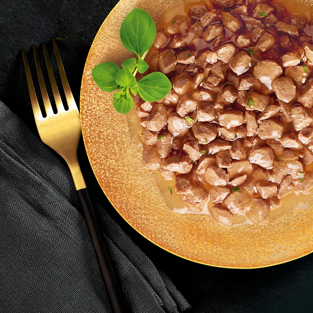 Gourmet-Katzenfutter auf einem Teller mit einer goldenen Gabel. Fleischstücke in Sauce mit Kräutern garniert.