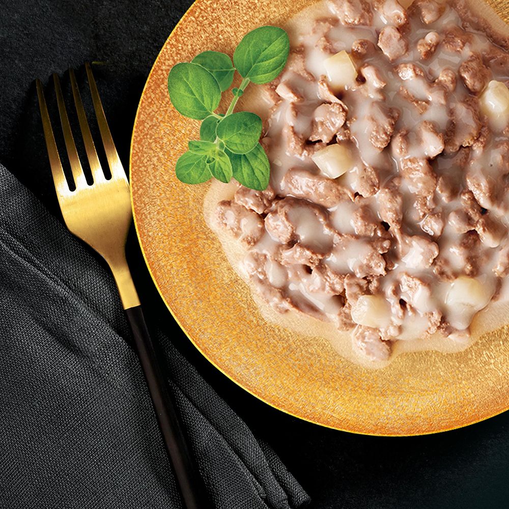 Gourmet-Katzenfutter auf einem Teller mit einer goldenen Gabel. Fleischstücke mit cremiger Sauce und Kartoffelstücken.