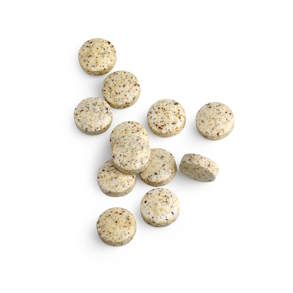 Mehrere Tabletten neben einer weißen Flasche mit Mo-Zyme. Tabletten sind beige mit dunklen Punkten.
