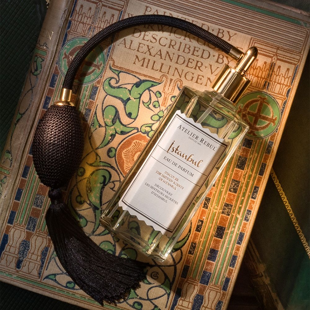 Eau de Parfum-Flakon mit Zerstäuber auf einem Buch. Goldfarbener Zerstäuber, schwarzer Balg. Aufschrift 'Istanbul'.