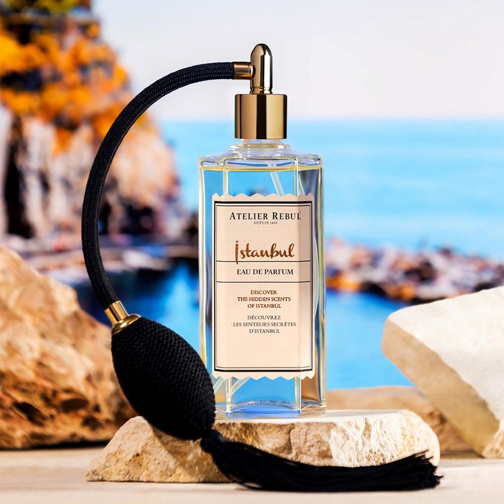 Eau de Parfum-Flakon mit Zerstäuber auf Steinen. Goldfarbener Zerstäuber, schwarzer Balg. Aufschrift 'Istanbul'.