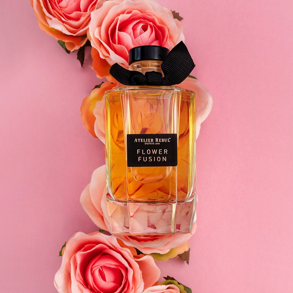 Glasflakon mit Duftflüssigkeit, umgeben von rosa und orangen Rosen.