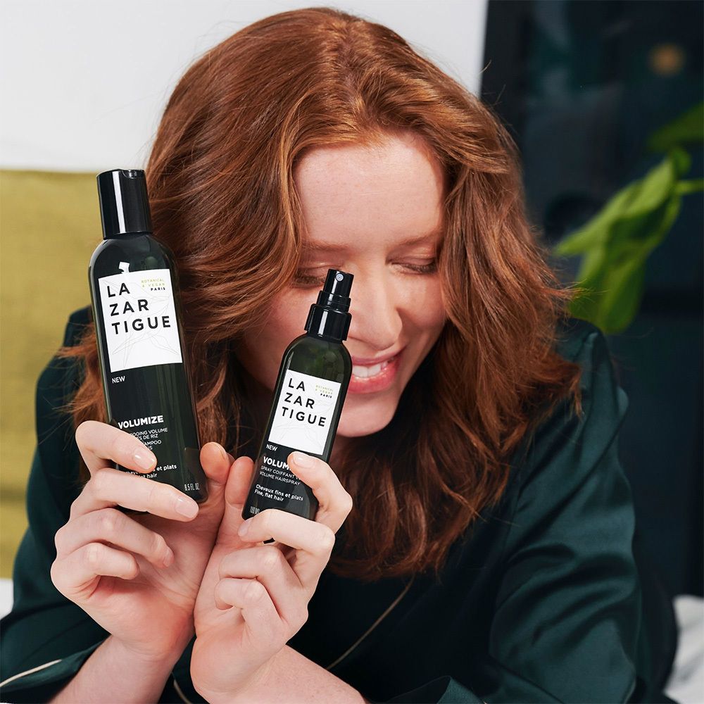 Frau hält zwei LAZARTIGUE VOLUMIZE Produkte. Eine große und eine kleine Flasche. Beide schwarz.