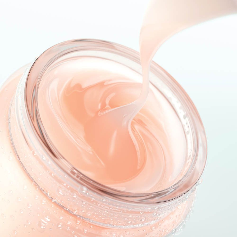 Ein Glas mit einer zartrosa Creme, die aus einem Spatel gegossen wird. Das Glas hat eine klare, runde Form mit Wassertropfen an der Außenseite.