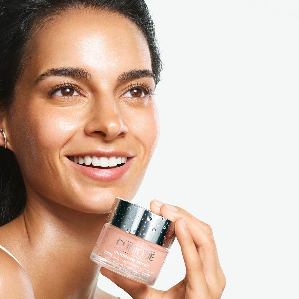 Frau hält Clinique Moisture Surge Tiegel mit silbernem Deckel und Wassertropfen.