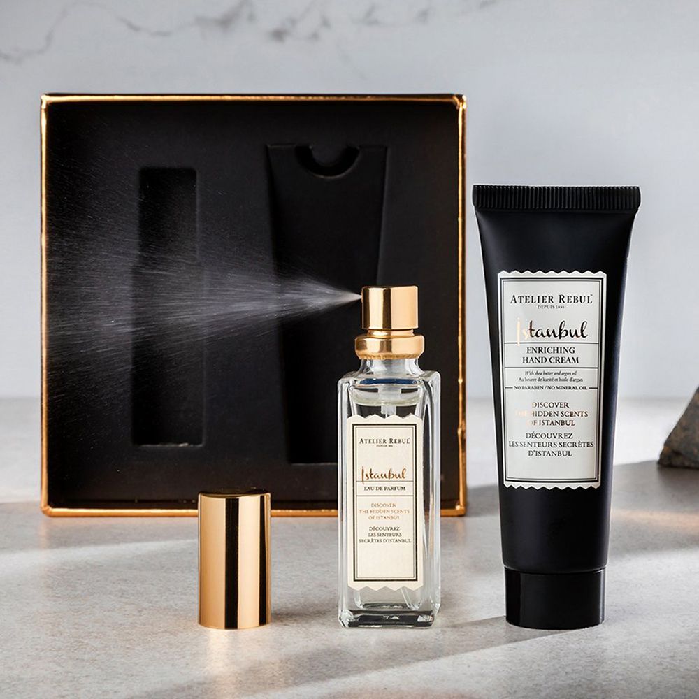 Flakon mit goldfarbenem Verschluss, Sprühnebel. Handcreme-Tube und schwarze Geschenkbox. Produktnamen und Marke sichtbar.