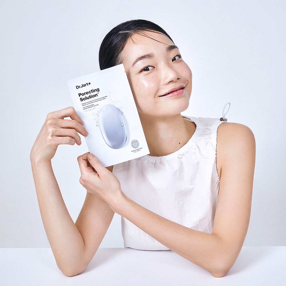 Frau hält Dr.Jart+ DERMASK™ Porecting Solution Maskenverpackung. Gesicht mit glänzender Haut. Weißer Hintergrund.