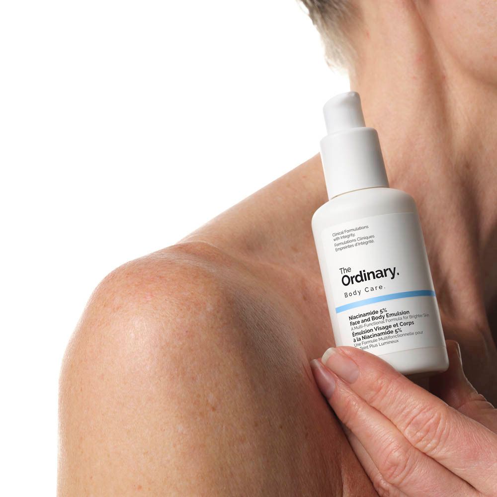 Weiße Flasche mit Pumpe. Aufschrift: The Ordinary. Niacinamide 5% Face & Body Emulsion. Gehalten von Person.