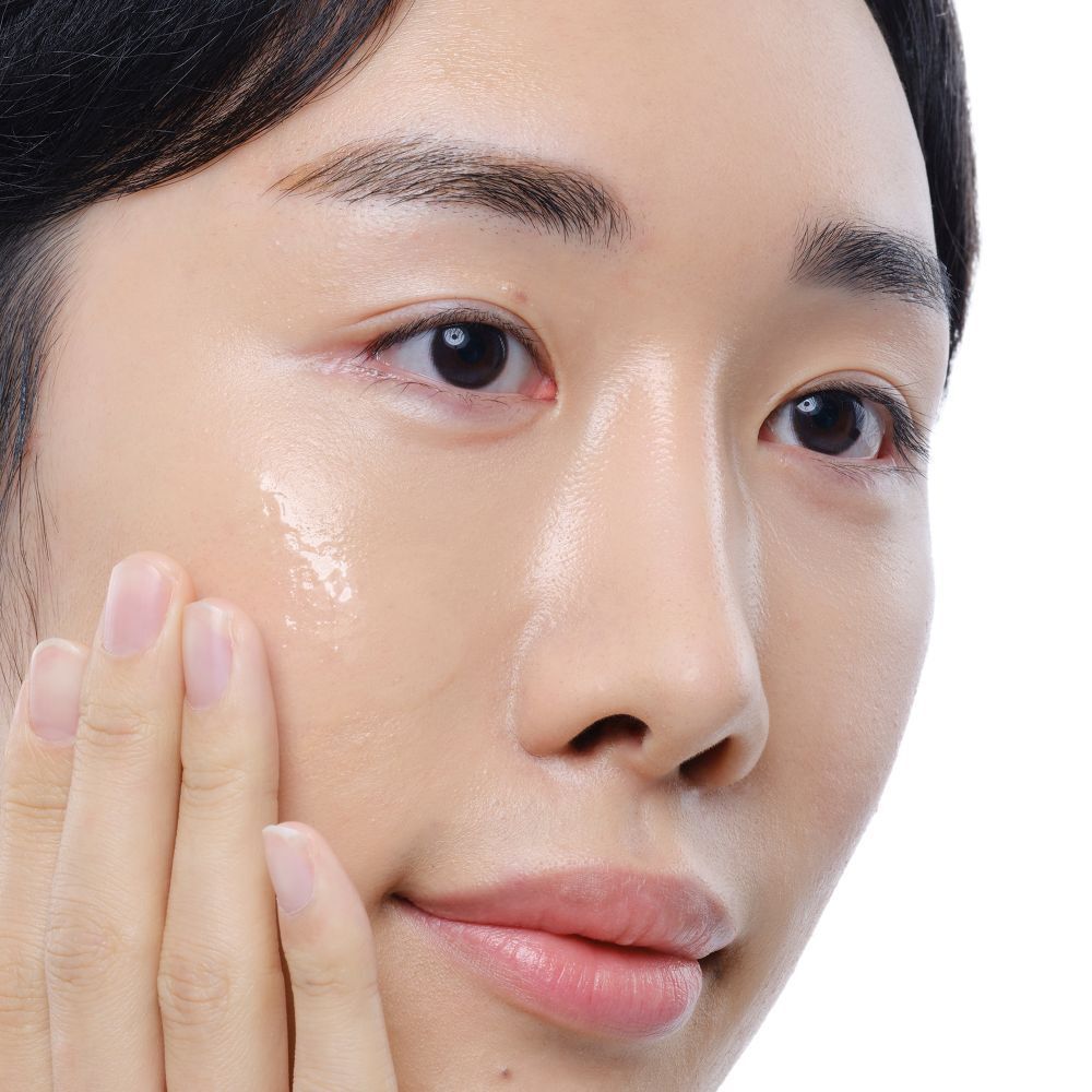 Gesicht einer Person. Haut mit aufgetragener, klarer Flüssigkeit. Hände berühren das Gesicht.