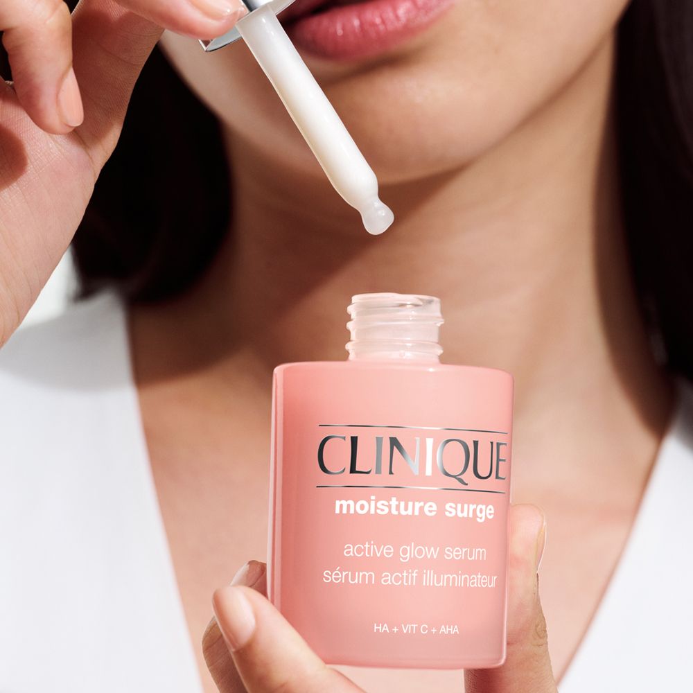 Rosa Flasche mit Tropfer. Schriftzug CLINIQUE, Moisture Surge, active glow serum. Tropfer wird gehalten.