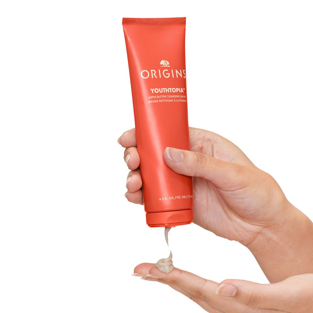 Hand hält rote Tube, aus der eine Creme auf einen Finger gedrückt wird.