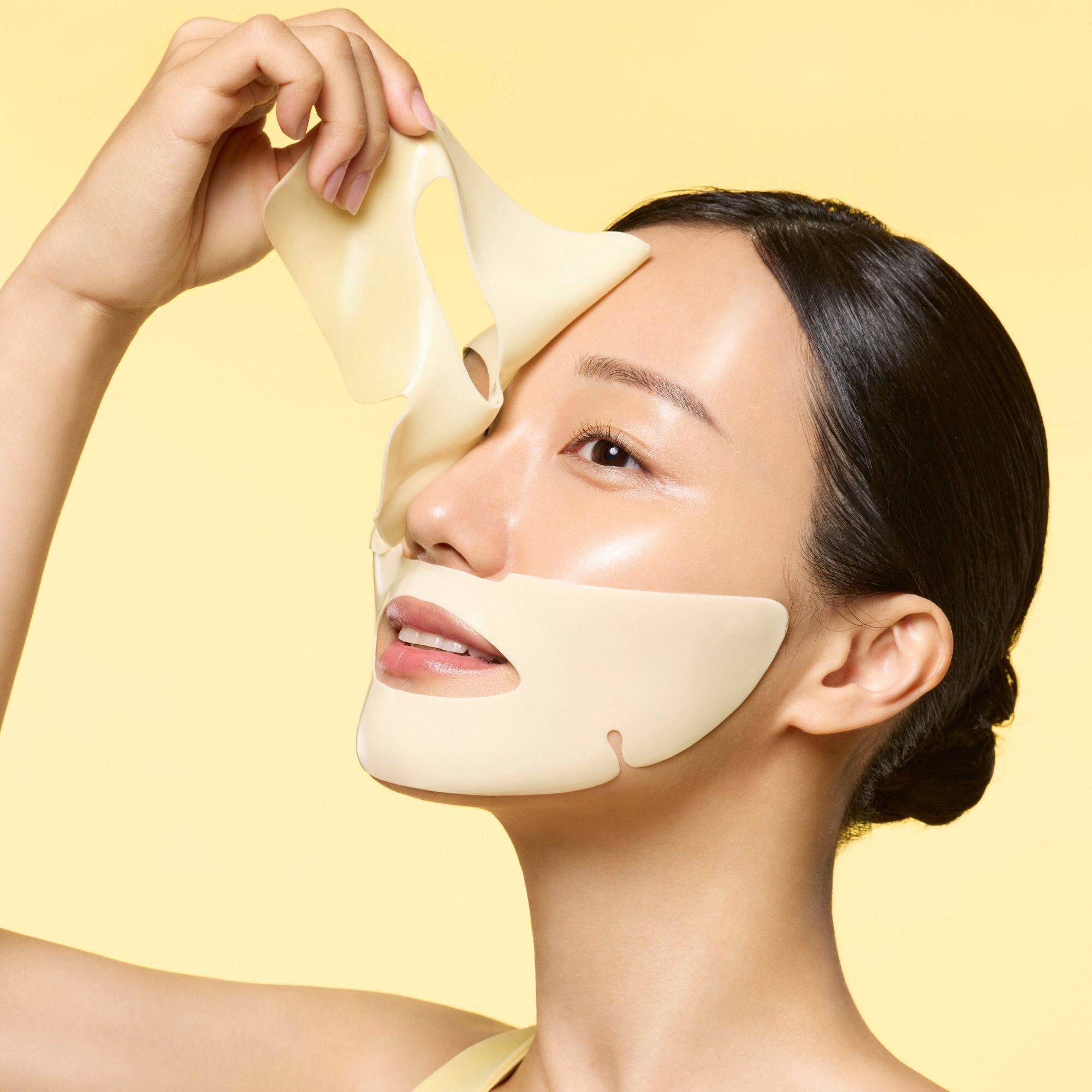 Eine Frau hält ein gelbes Maskenblatt von Dr.Jart+ Cryo Rubber™ Brightening Mask an ihr Gesicht.