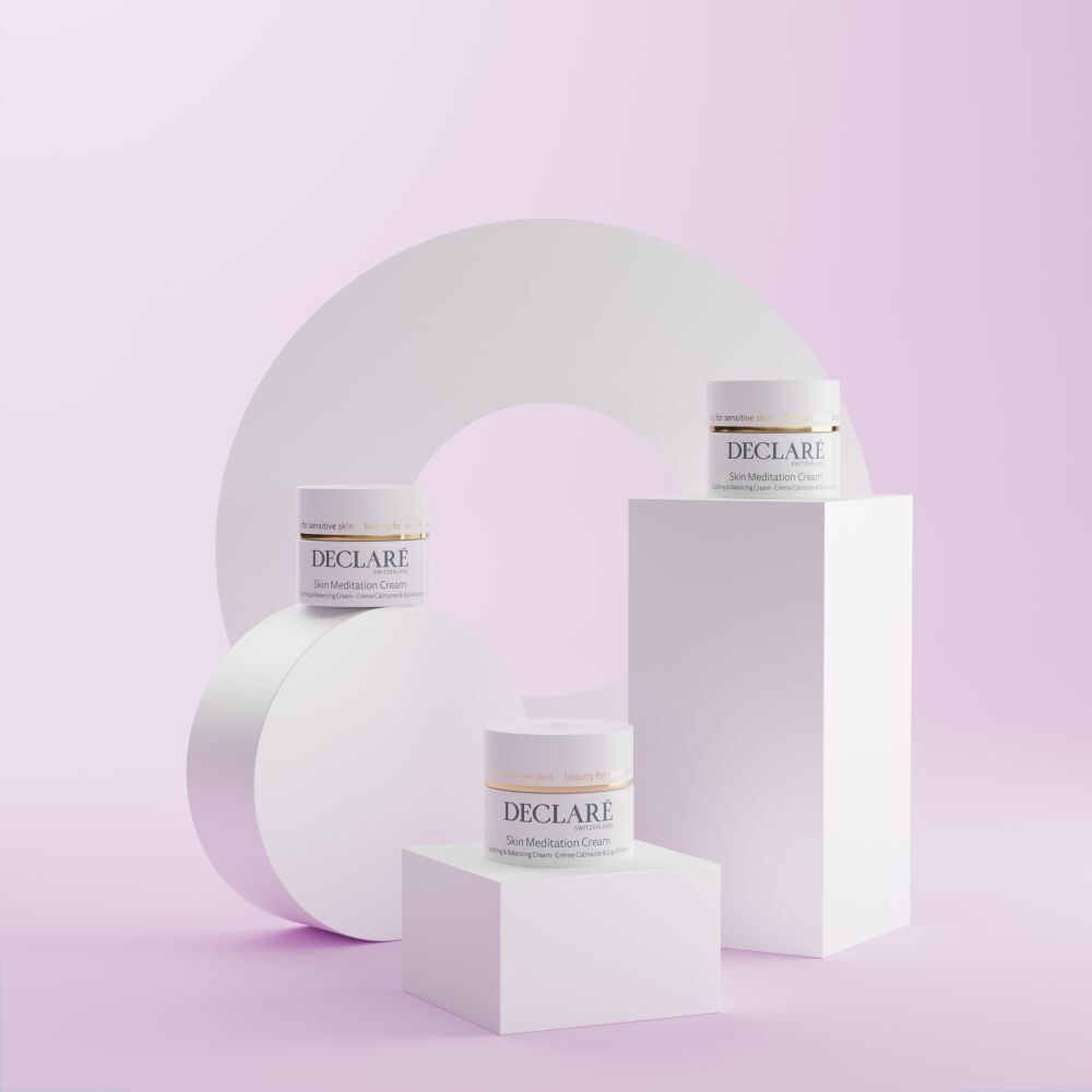 Drei Creme-Tiegel auf Podesten. Hintergrund mit weißem Kreis und rosa Elementen. Aufschrift: DECLARÉ Skin Meditation Cream.
