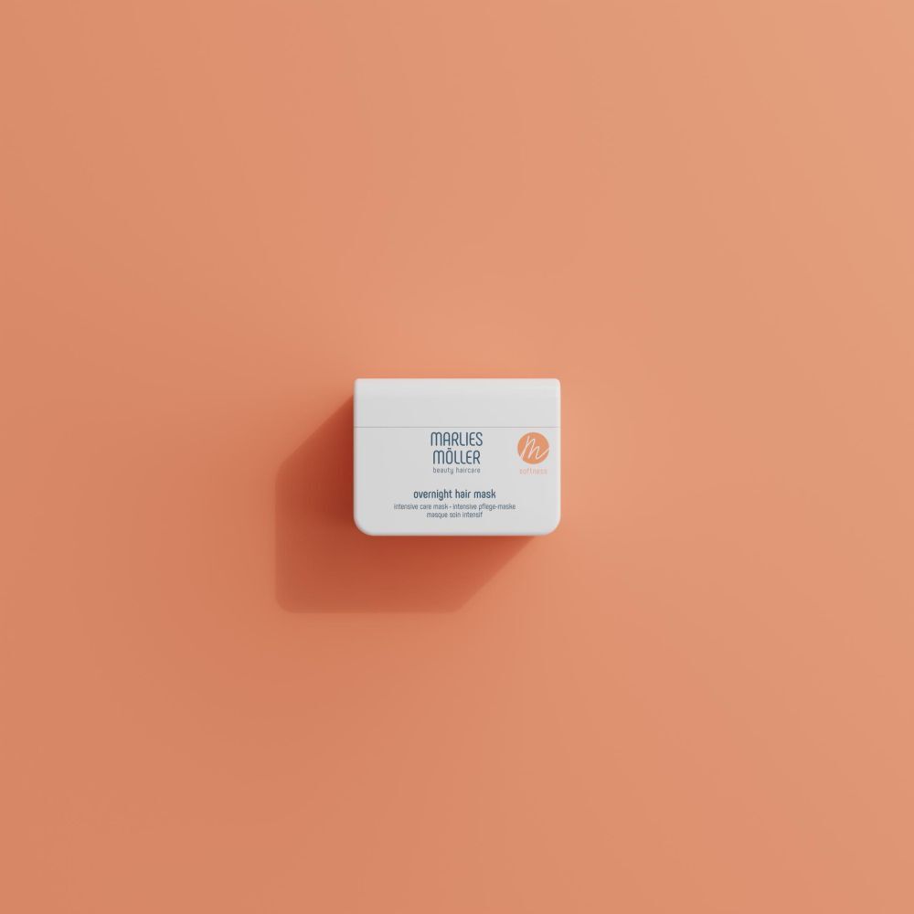 Weißer Behälter mit Marlies Möller Overnight Hair Mask, auf orangefarbenem Hintergrund. Draufsicht.