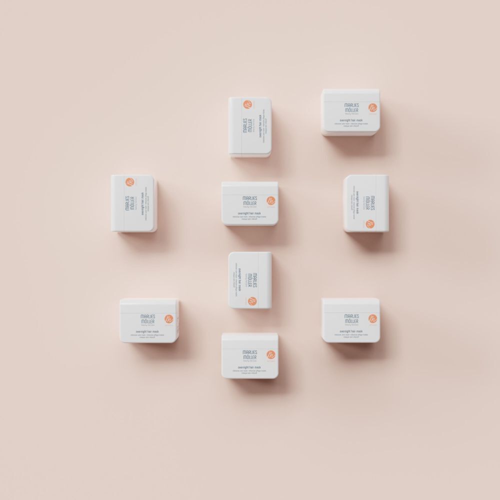 Mehrere weiße Behälter mit Marlies Möller Overnight Hair Mask, auf rosa Hintergrund. Draufsicht.