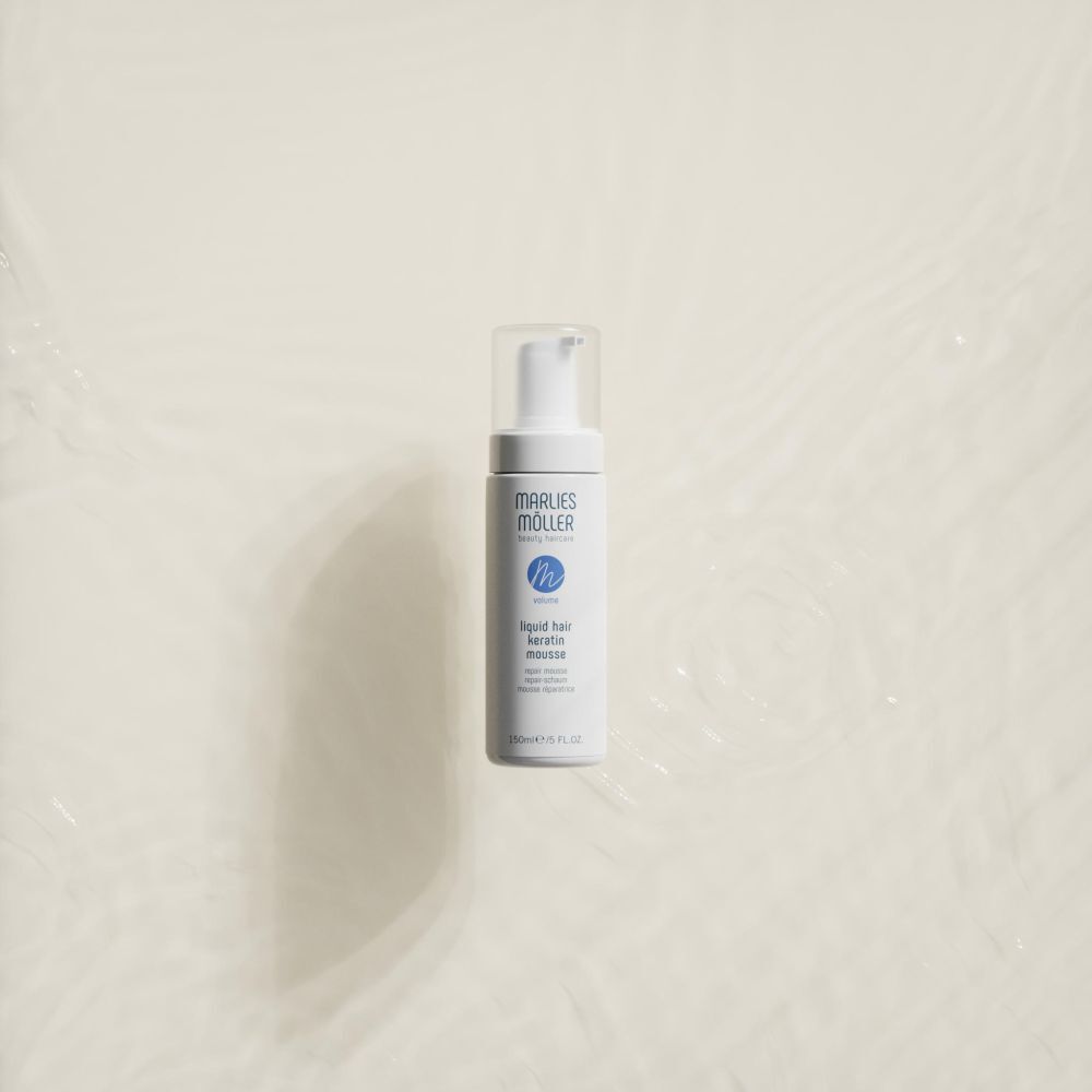 Weiße Flasche mit Sprühkopf. Aufschrift: Marlies Möller, beauty haircare, Volume, Liquid Hair Keratin Mousse. Auf hellem Hintergrund.