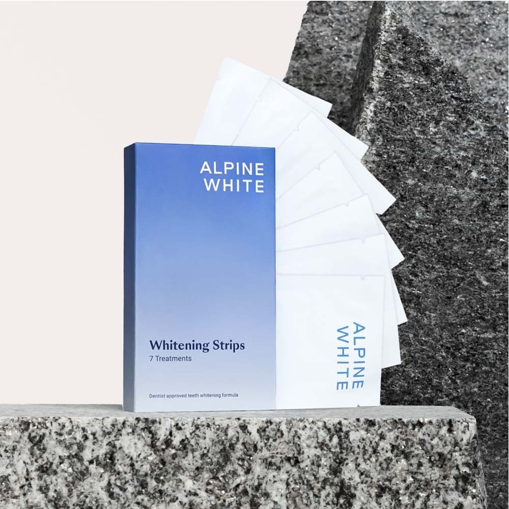 Blau-weiße Schachtel mit ALPINE WHITE und Whitening Stripes. 7 Behandlungen. Auf Stein platziert.