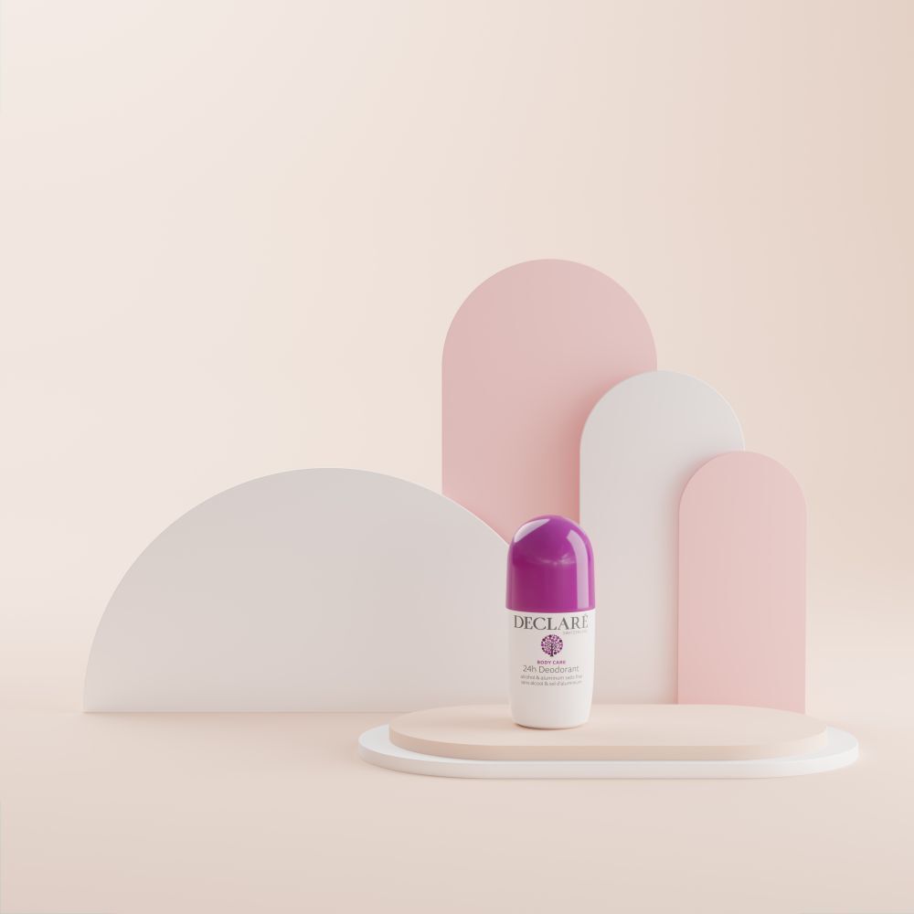 Roll-on-Deo auf Podest. Weißes Gehäuse, lila Kappe. DECLARÉ, 24h Deodorant. Hintergrund: rosa, weiße, geschwungene Formen.