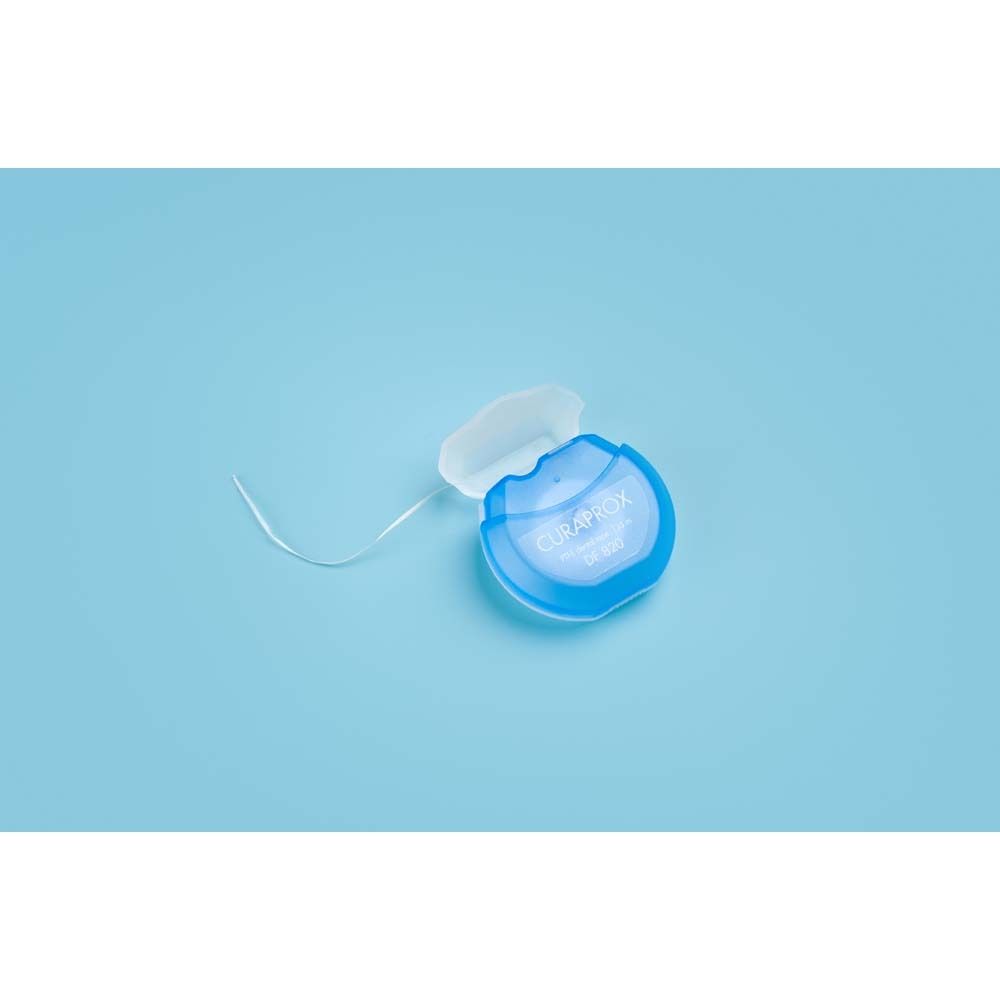 Blauer Zahnseide-Spender mit weißer Kappe. Faden ist sichtbar. Auf blauem Hintergrund.