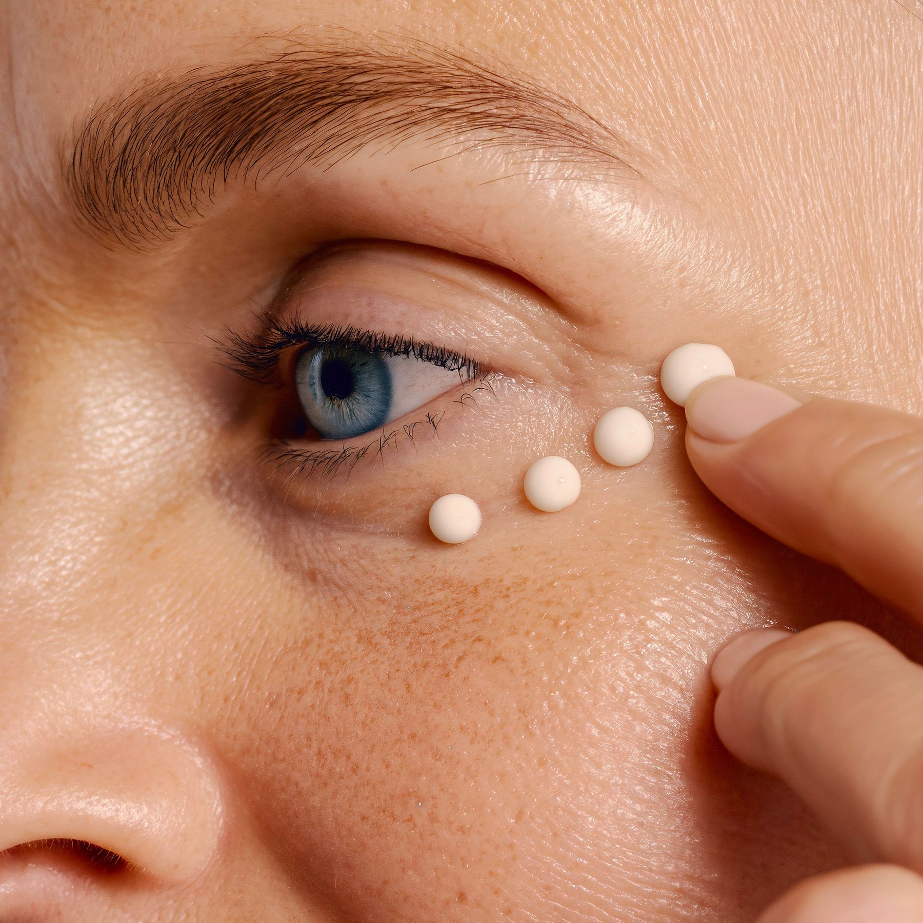 Nahaufnahme eines Auges mit Creme-Punkten. Keine Produktnamen sichtbar.