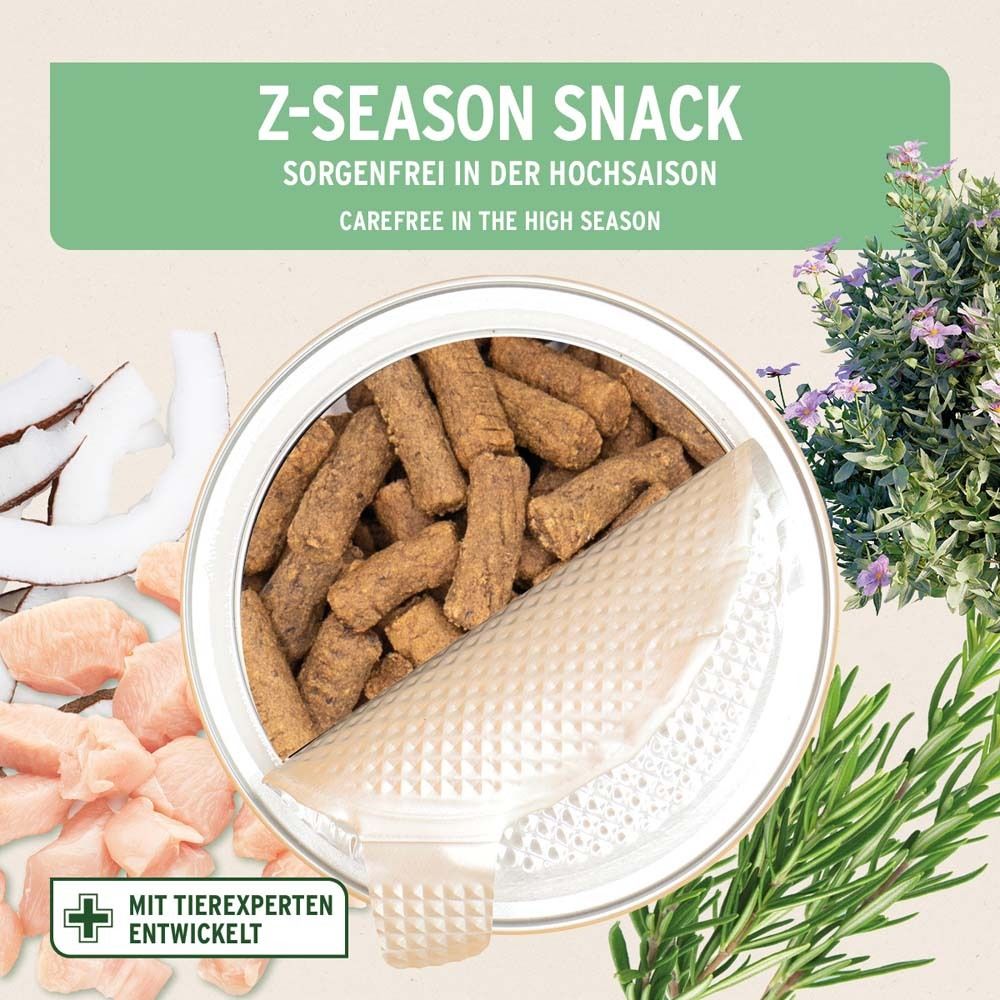 Geöffnete Dose mit Z-Season Snack. Braune, längliche Snacks. Kokosnuss, Hühnchen und Kräuter als Dekoration.