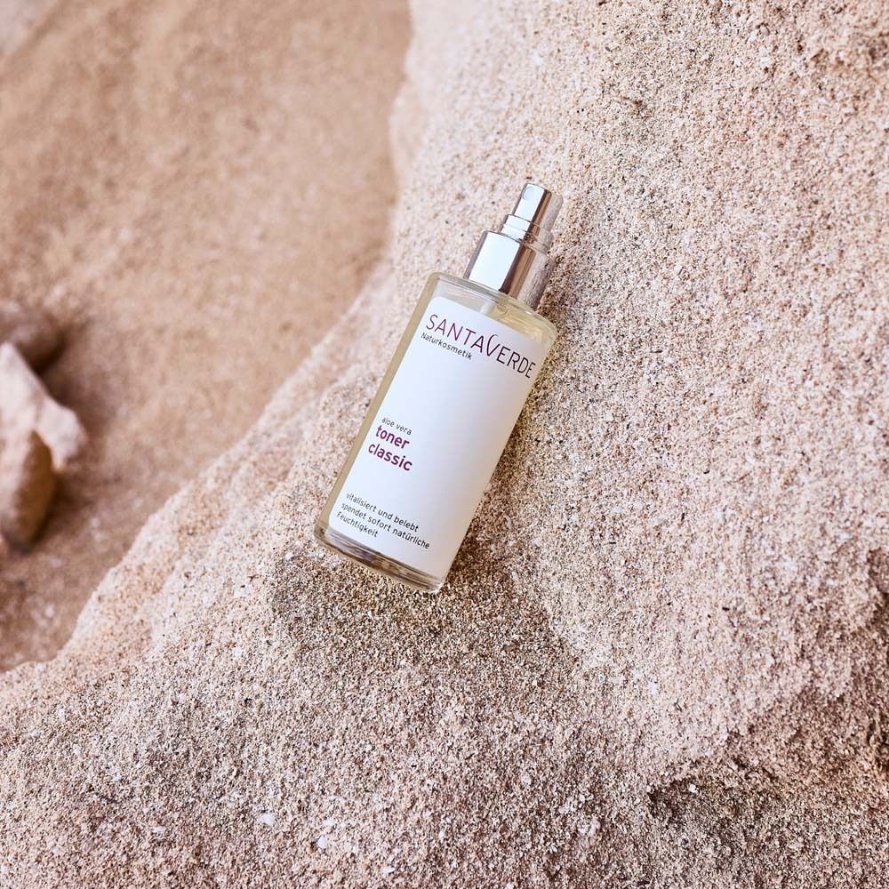 SANTAVERDE Aloe Vera Toner Classic. Glasflasche mit Sprühkopf auf Sand. Produktetikett mit Produktnamen.