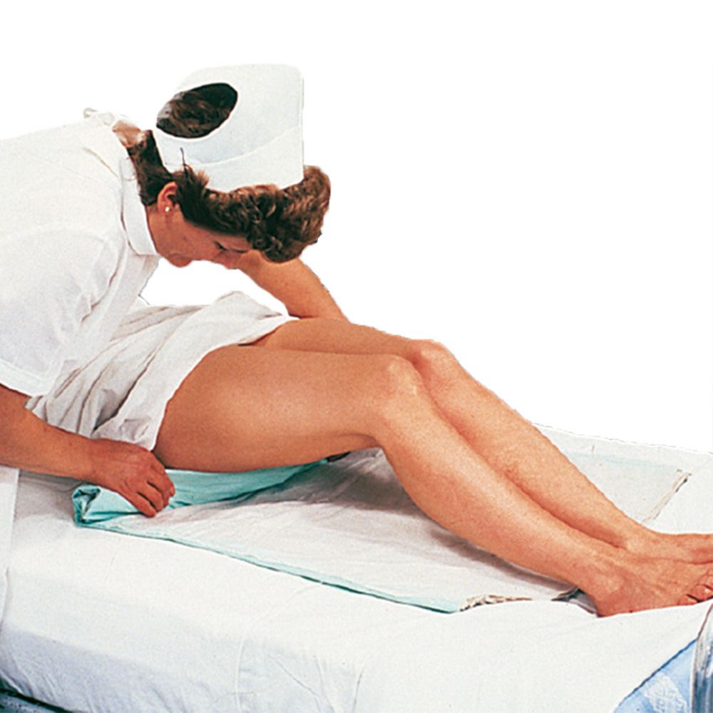 Eine Pflegekraft legt eine grüne Krankenunterlage unter die Beine einer Person, die auf einem Bett liegt.