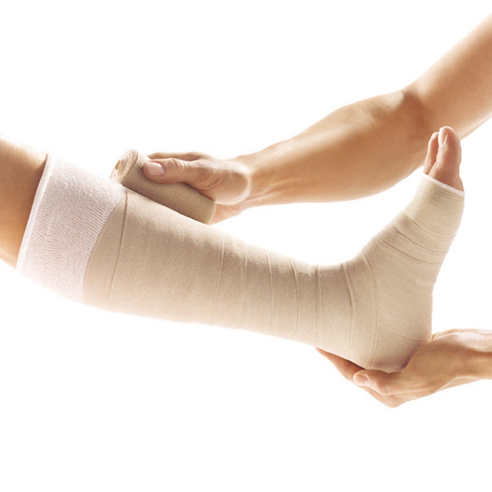 Bein mit Bandage. Eine Hand hält das Bein, die andere wickelt Bandage. Beige Bandage um Fuß und Unterschenkel.