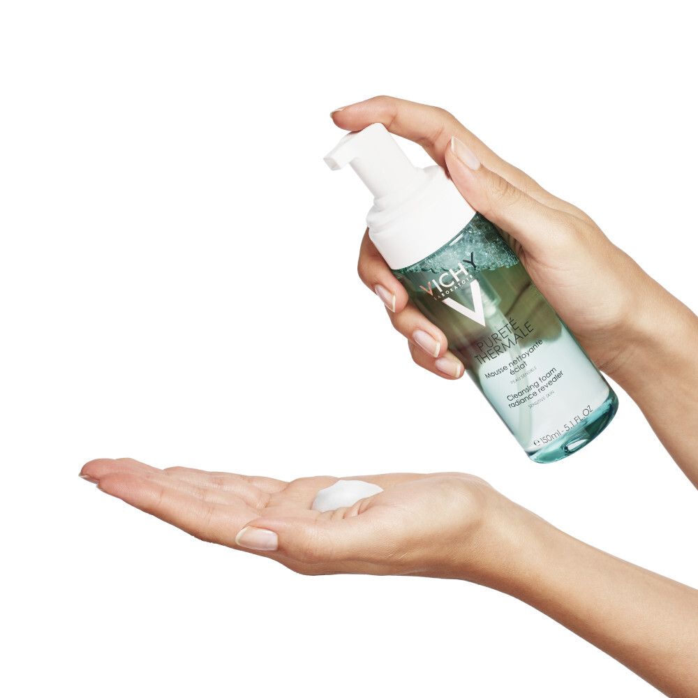 Hände halten Vichy Pureté Thermale Flasche. Schaum wird in die Handfläche gesprüht.
