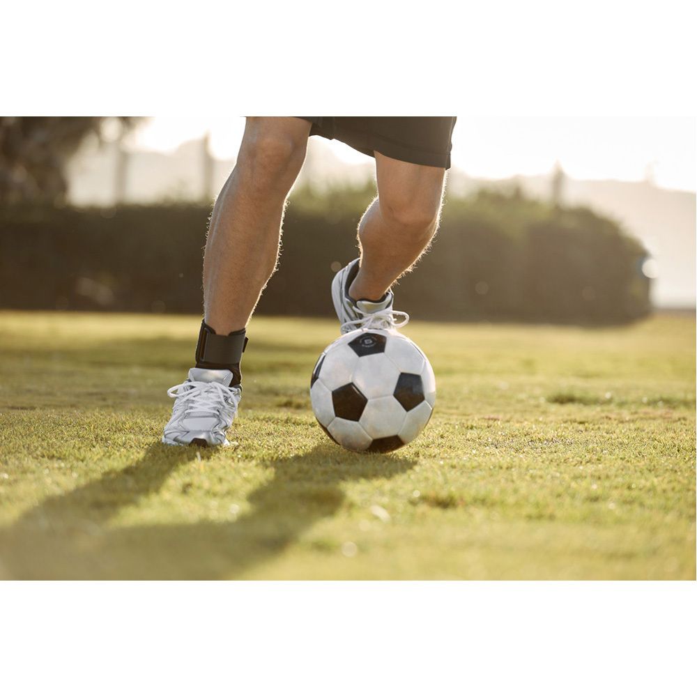Fußballspieler mit FUTURO Sport Deluxe Sprunggelenk-Bandage. Schwarze Bandage am Fuß, Fußball. Auf Gras.