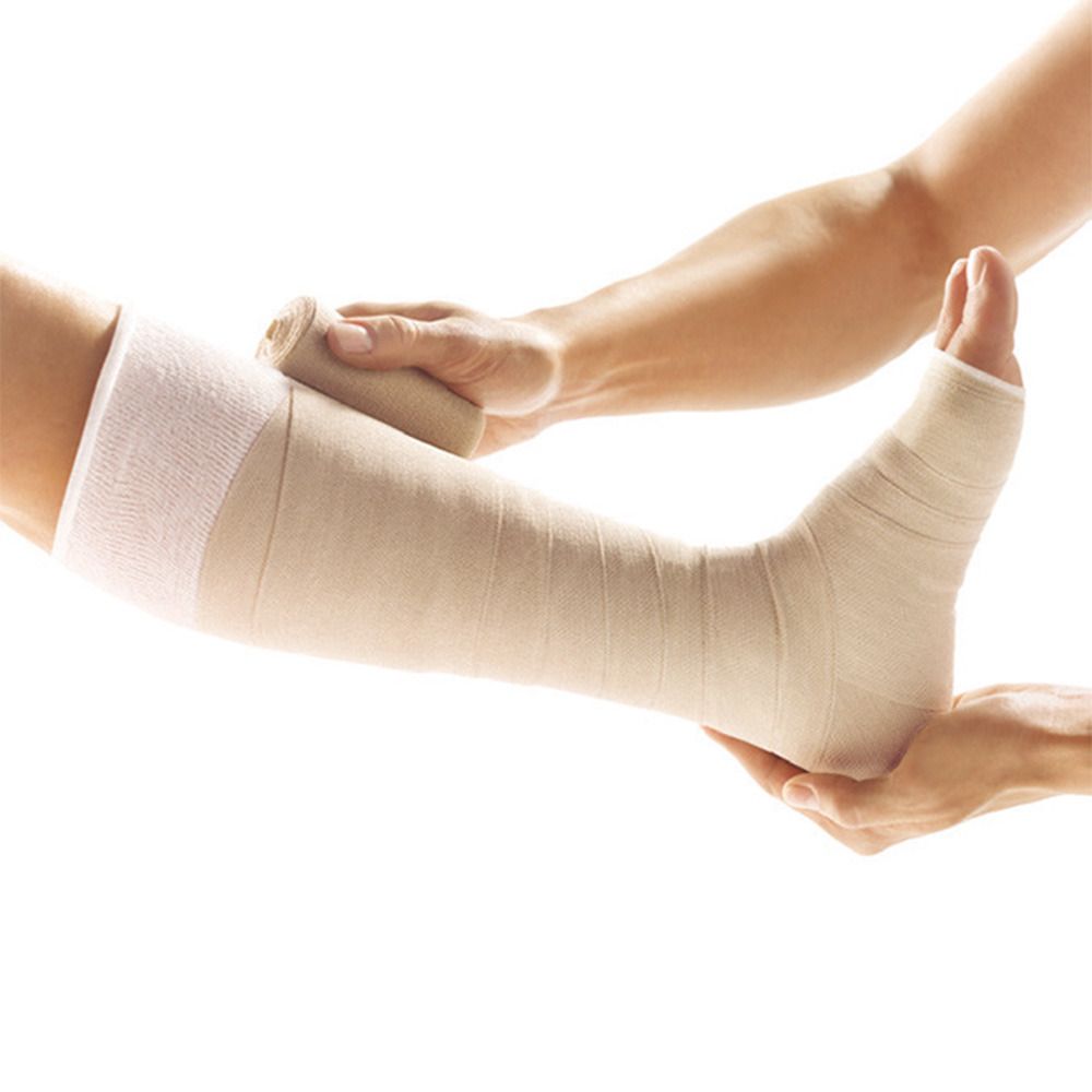 Bein mit Bandage. Ein Arm hält den Fuß, ein anderer wickelt die Bandage. Beige Bandage, weißer Strumpf.