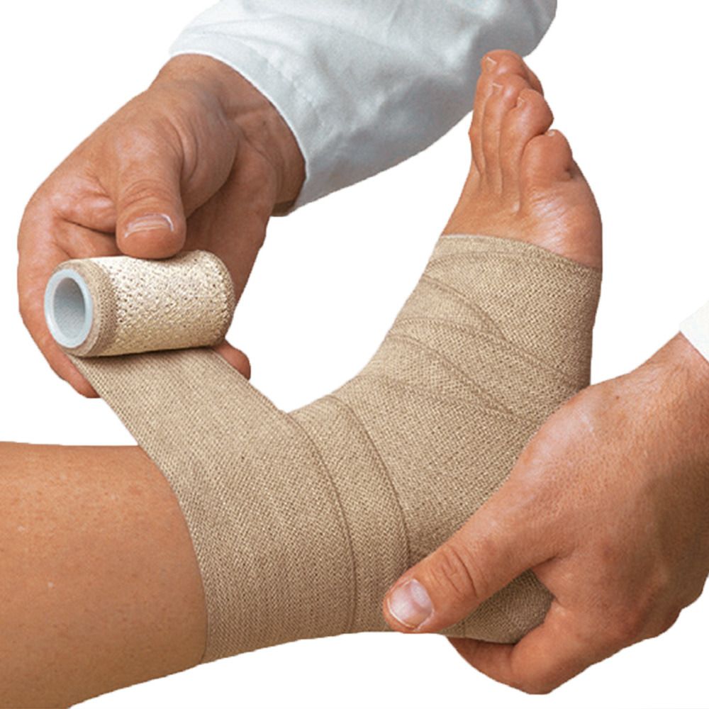 Beige elastische Bandage wird um einen Knöchel gewickelt. Eine Hand hält die Rolle, die andere wickelt die Bandage.