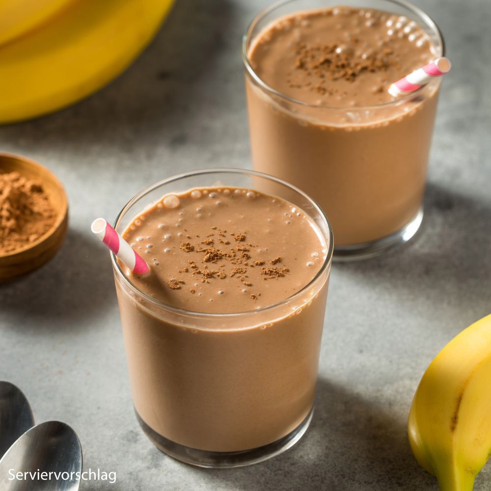 Zwei Gläser Schokoladengetränk mit Strohhalmen. Bananen im Hintergrund. Servierbeispiel.